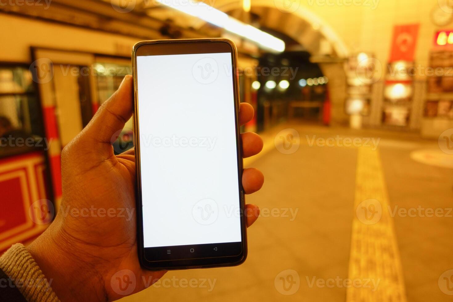 Hand holding smartphone in subway station at night photo