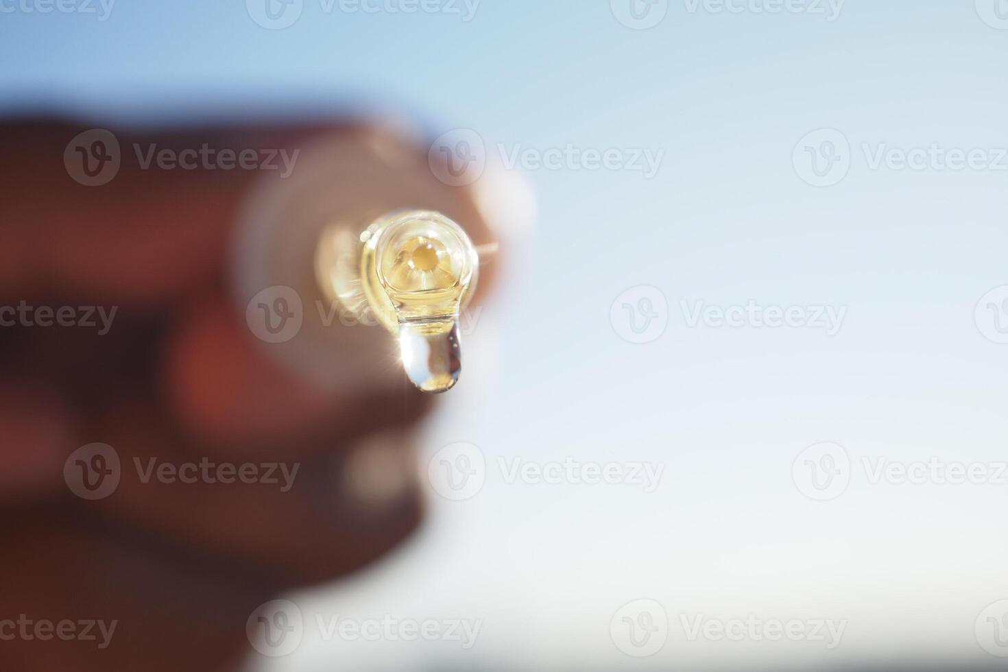 A person holds a dropper tube with aessential oil drop glistening in sunlight photo