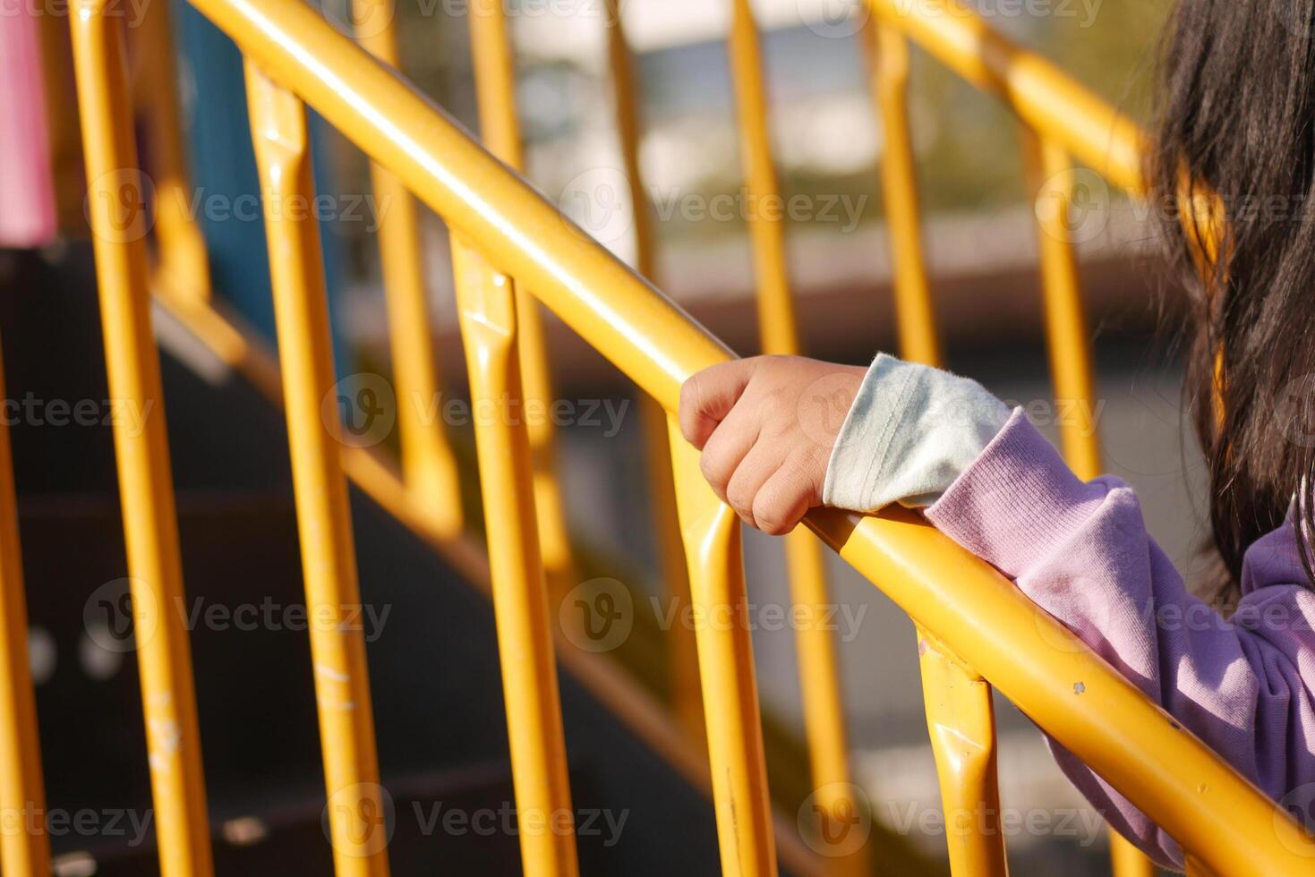 Child grips yellow railing at playground afternoon photo