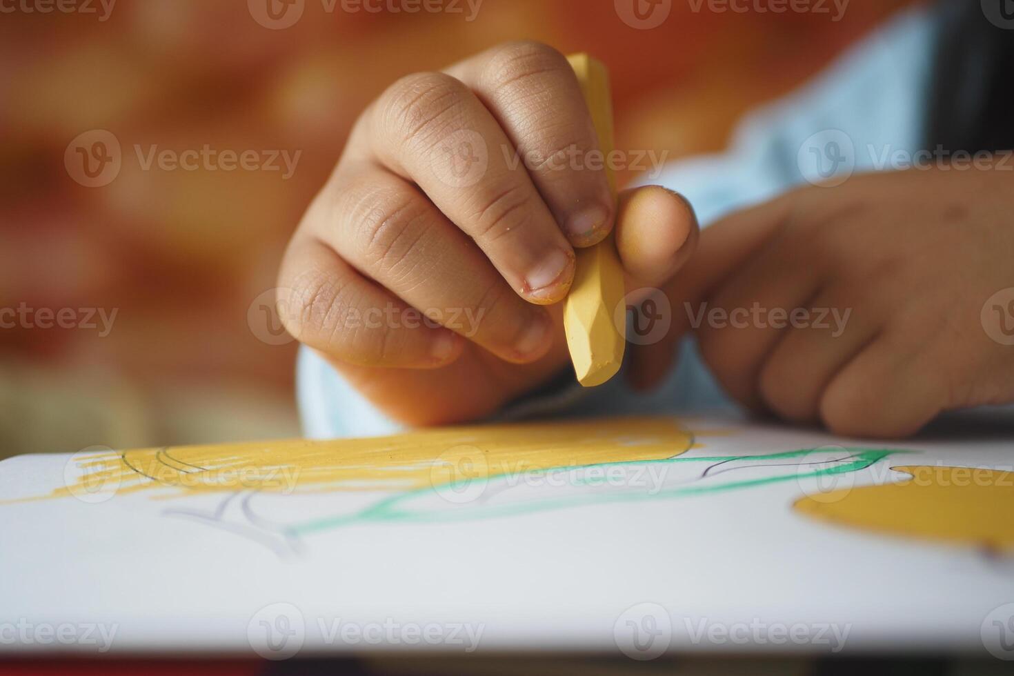 Child creating art with yellow crayon on white paper photo