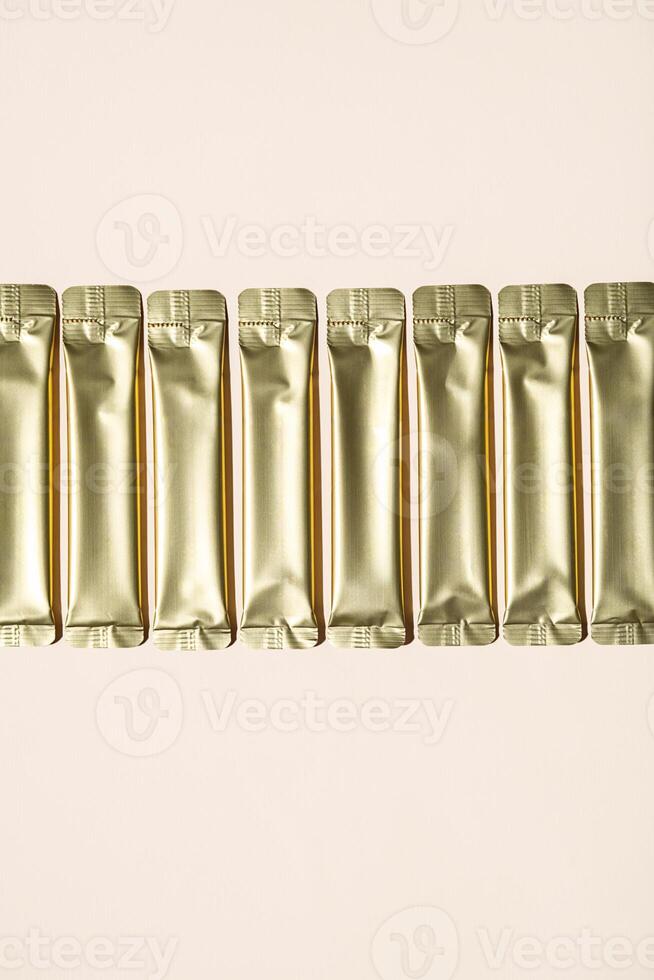 Row of Several Shiny Golden Sachets on a Light Background. Packaging for Powder Products. photo