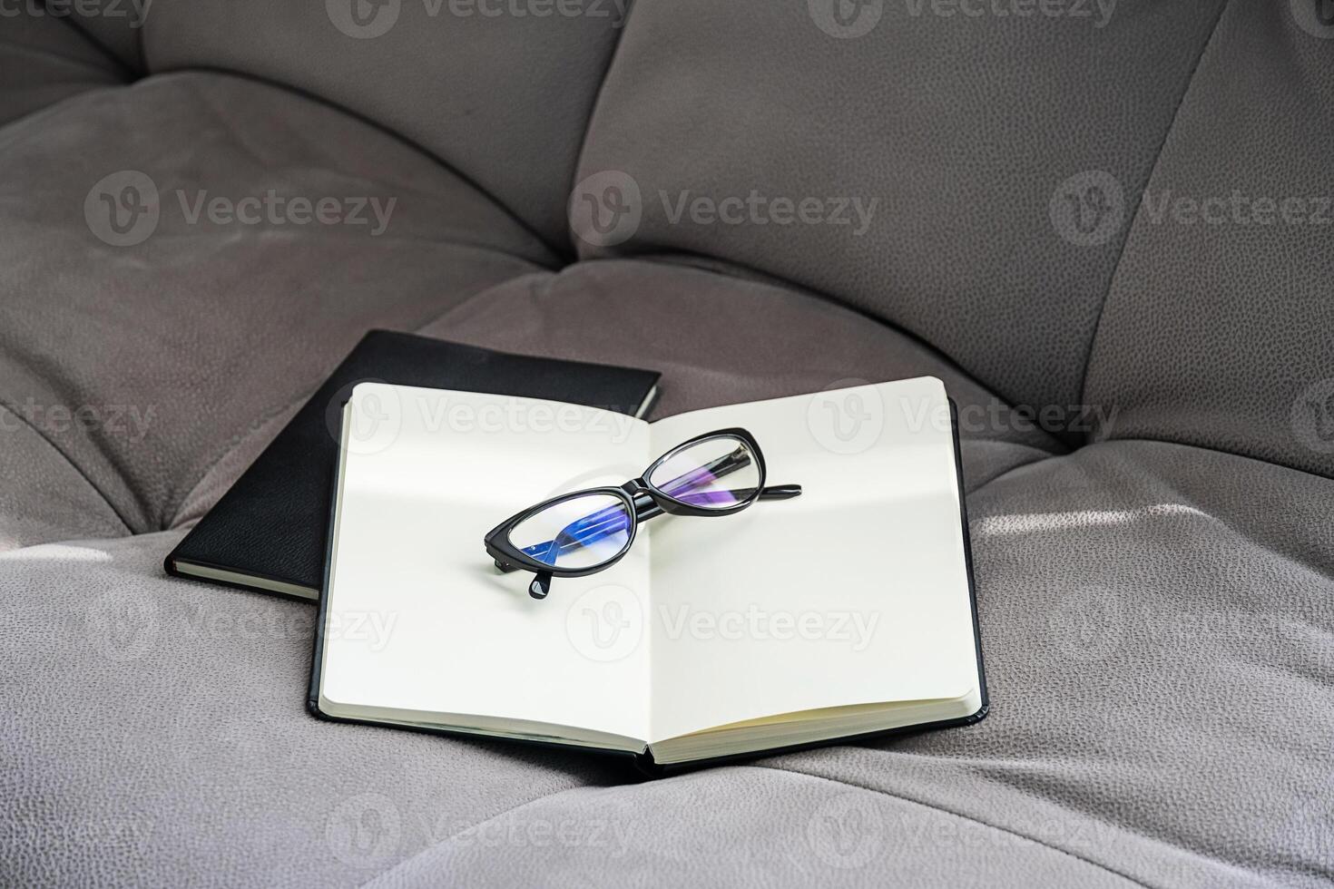Open Notebook with Blank Pages and Pair of Glasses Rests on a Gray Couch. photo