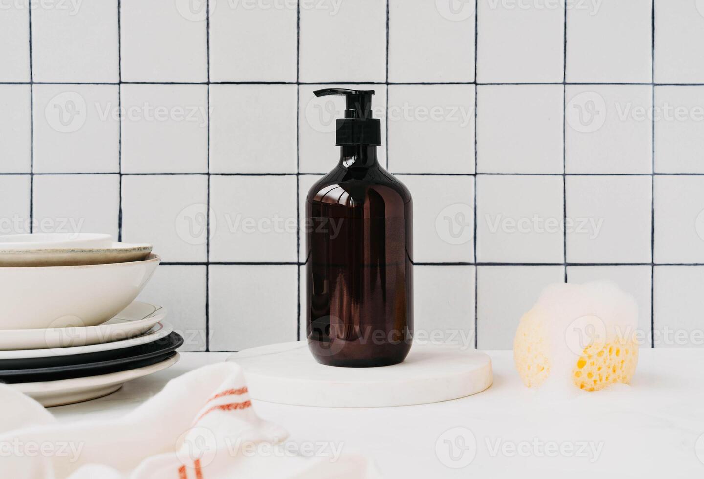 Bottle with dish detergent on marble podium with clean plates and sponge with foam photo