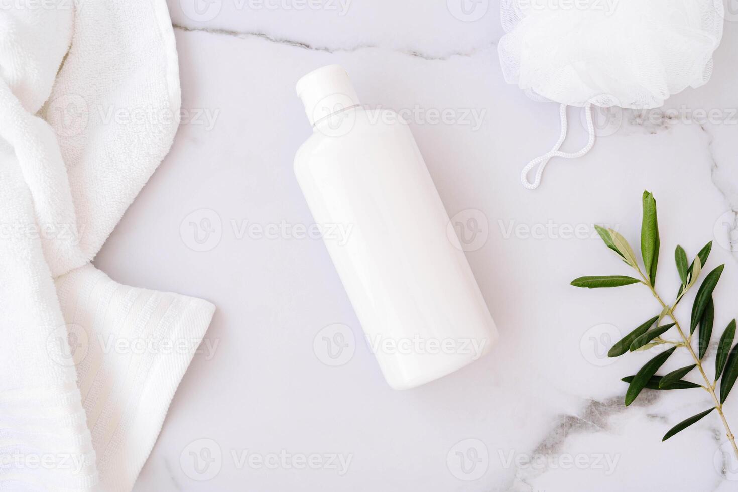 Flat lay of white plastic bottle without label, sponge for body, towel and olive branch on white bath marble background photo