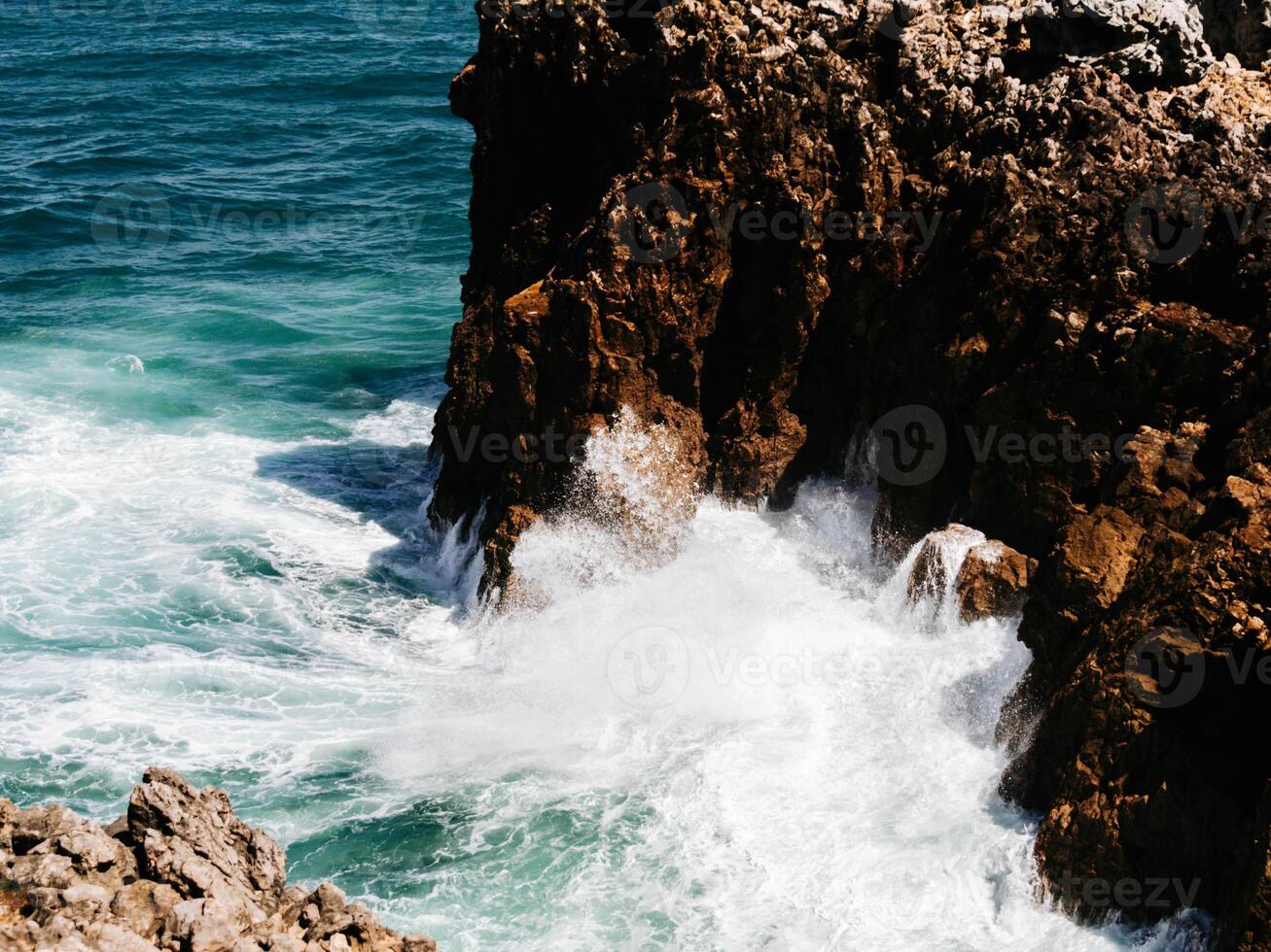Top view from above of the ocean waves crashing against the brown textured rocks photo