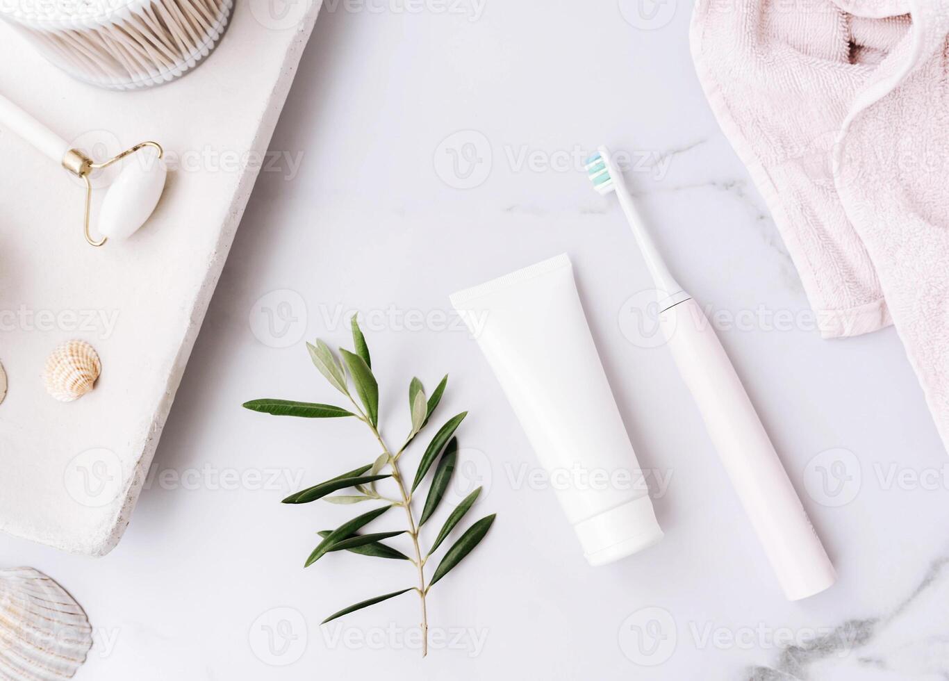 Top view of white tube without label, electric toothbrush and olive branch on white bath background photo