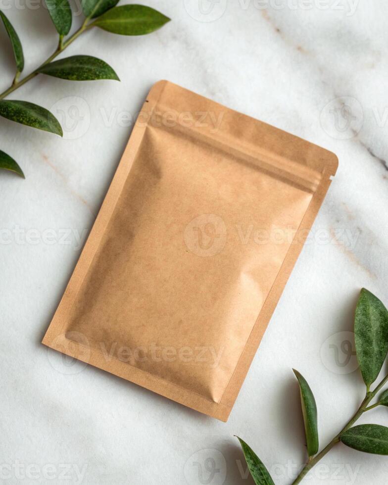 Brown paper bag with green leaves on a white marble background photo
