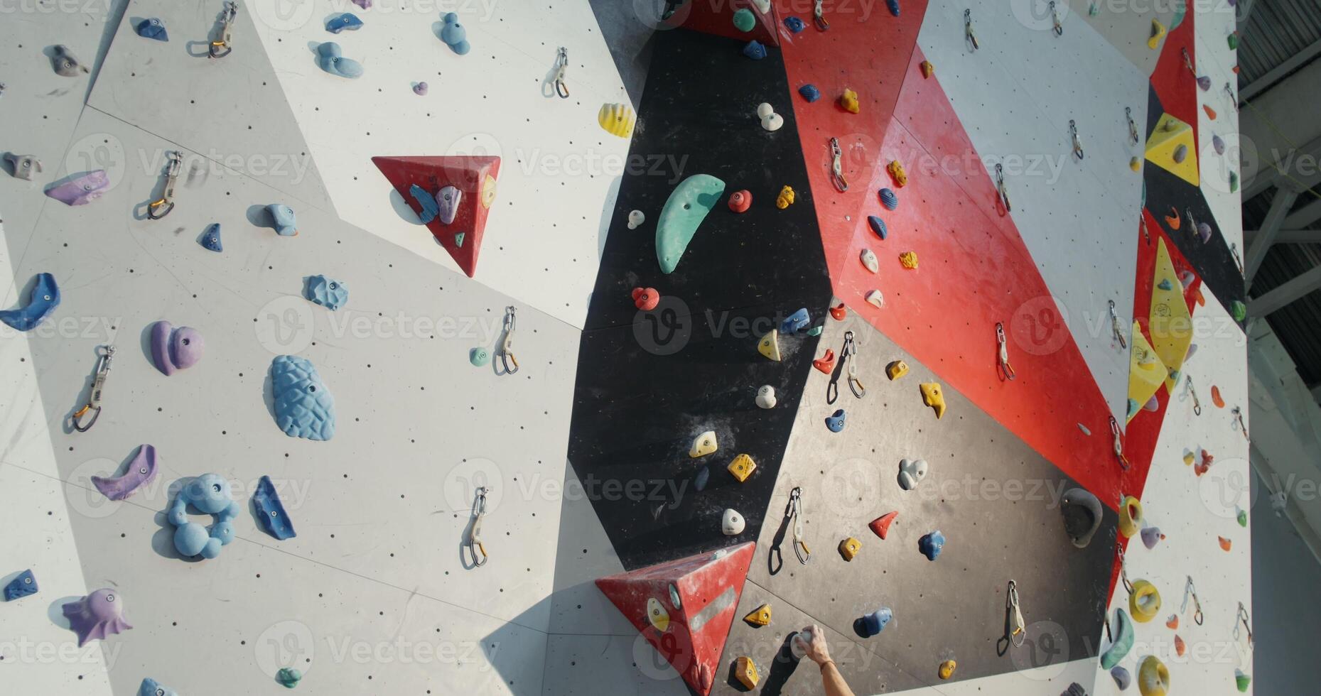 Young man of European appearance climbs up the indoor climbing wall without safety ropes. Preparation of mountaineers in a modern sports hall photo