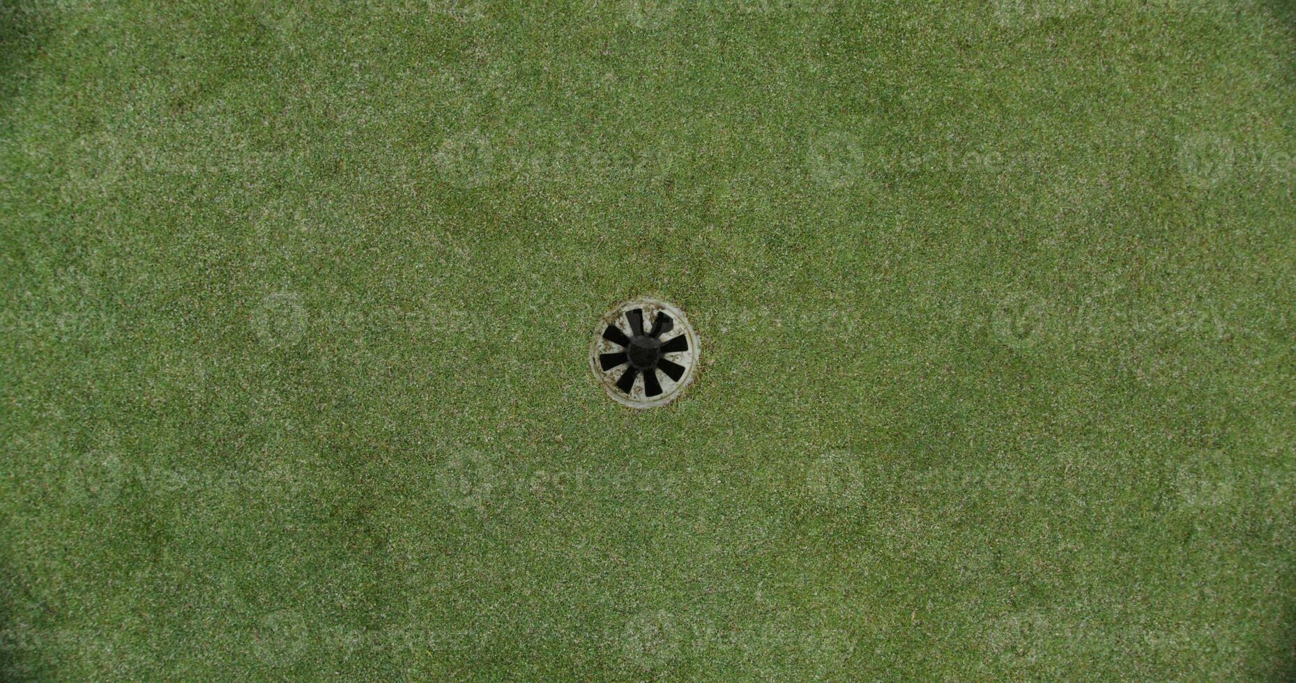 View of a golf course set on artificial turf. The golf ball rolls up to the hole and spins around its circumference photo