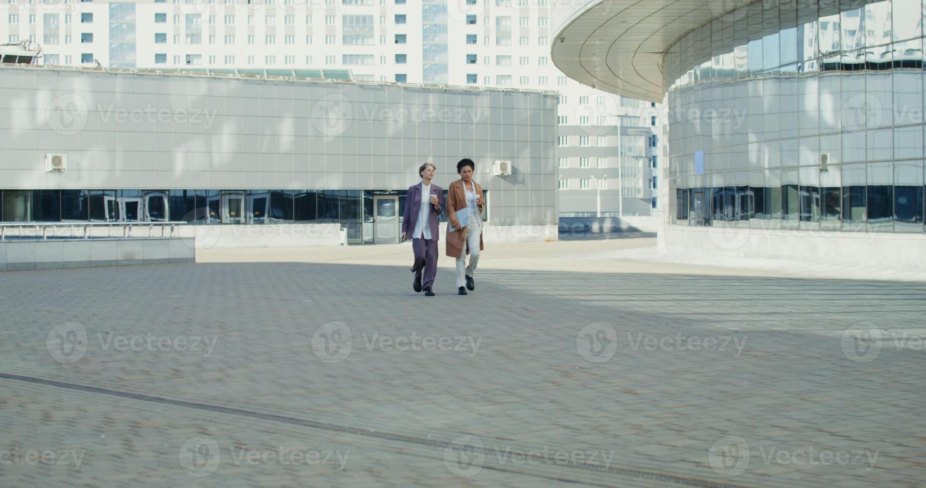 Business women talking to each other and drinking coffee while walking through the business center of a modern city, on a sunny autumn day photo