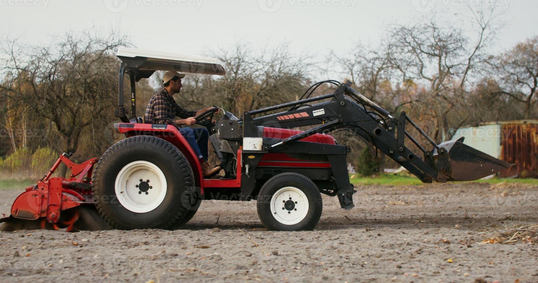 Young male tractor driver drives a modern multipurpose agricultural machine plowing a field on an autumn day. Side videography photo