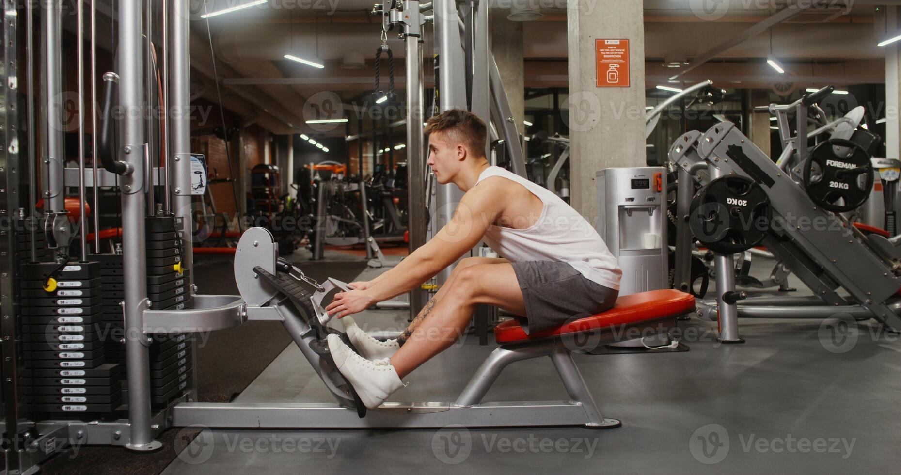 A young man, athletic physique is engaged in the gymnasium, doing exercises to look at the muscles of the chest on a modern simulator. Side videography photo