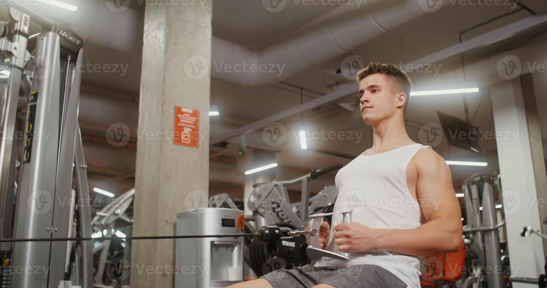 Sportive young man of European appearance is engaged in a simulator for exercises on the muscles of the chest, lifting weights with his hands, sitting on a bench in a modern gym photo