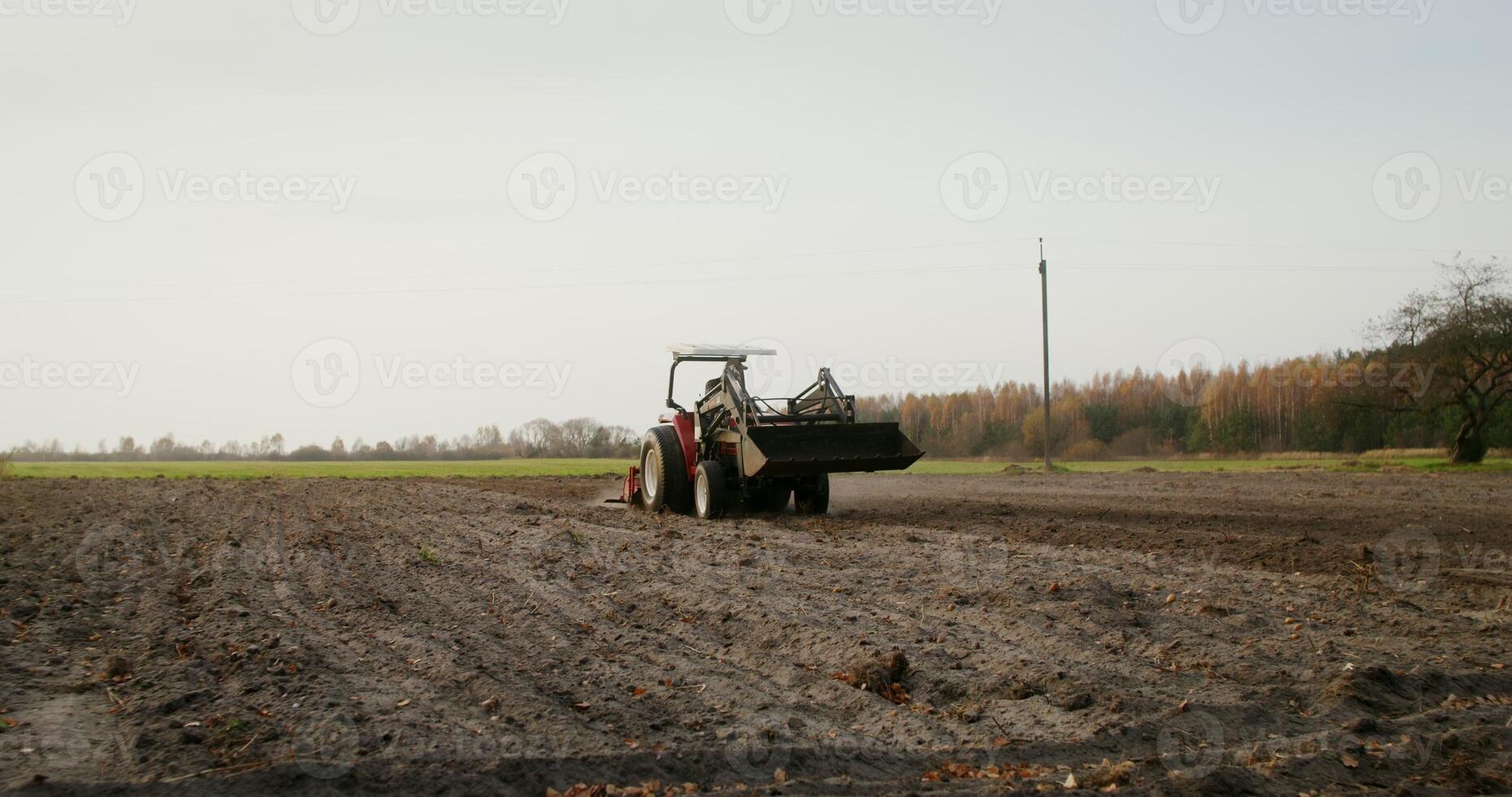 Young farmer of European appearance drives an agricultural tractor across a field on an autumn day, leaving behind even rows of plowed land photo
