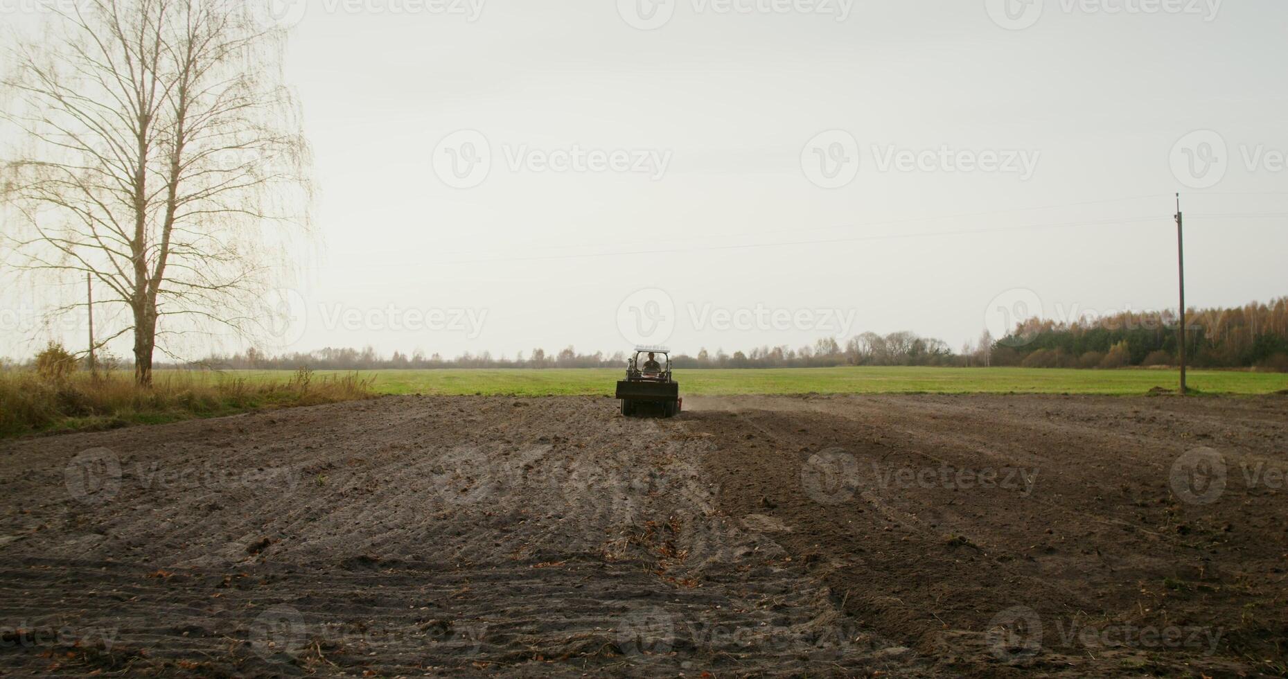 Male tractor driver drives an agricultural tractor plowing a small field on a fine autumn day. Filming from afar photo