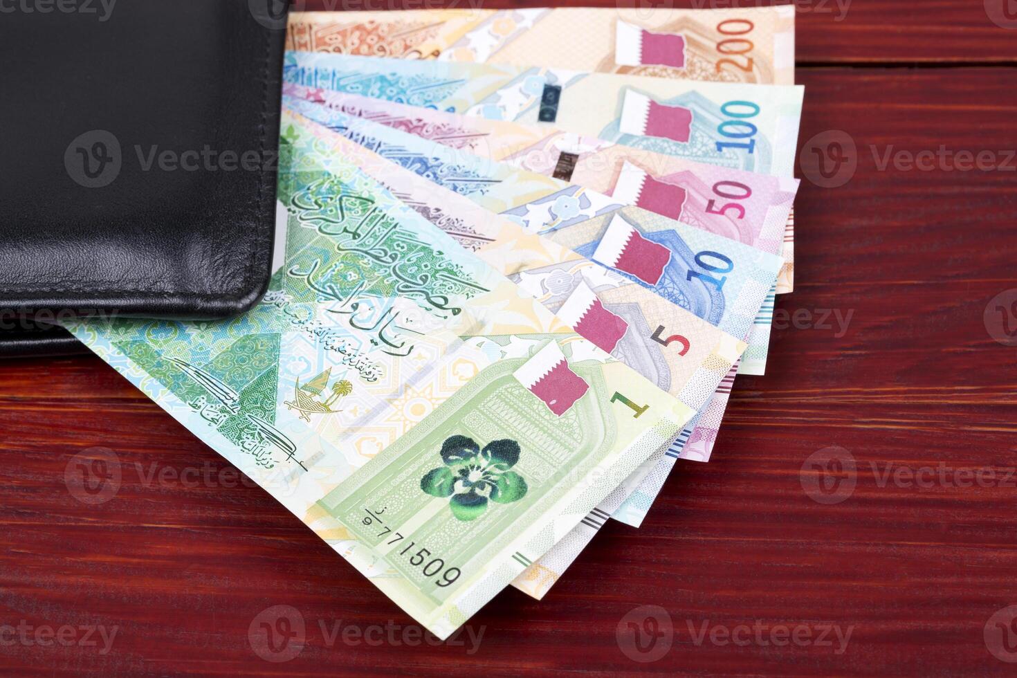 Qatari Riyal in the black wallet on a wooden background photo