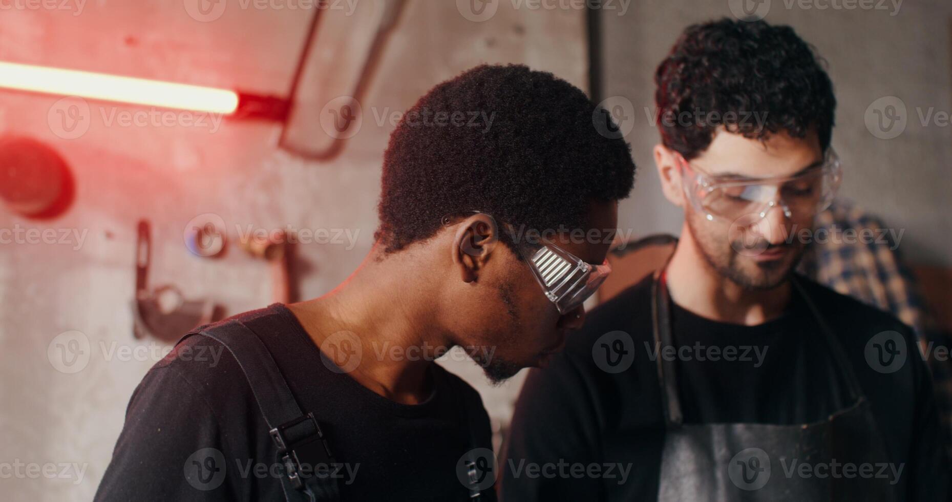 Two blacksmiths of different nationalities in work clothes are considering a sketch of a future product, working together and using a tablet, close-up. 4k , red komodo photo