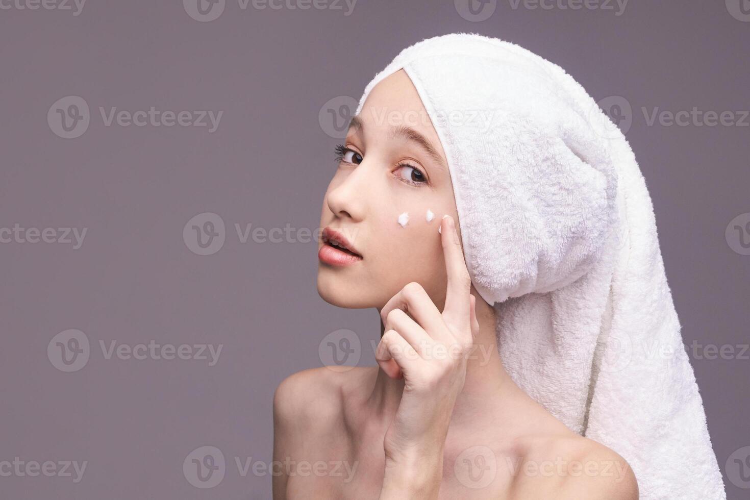 Young caucasian female applying skincare with towel wrapped hair. photo