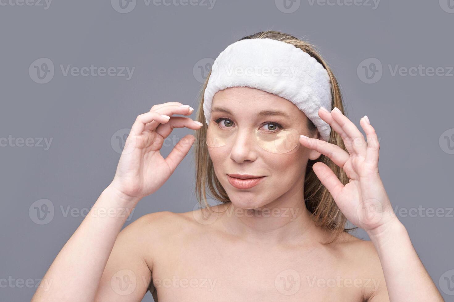 Young caucasian female applying under eye patches for skincare routine with relaxed expression. photo