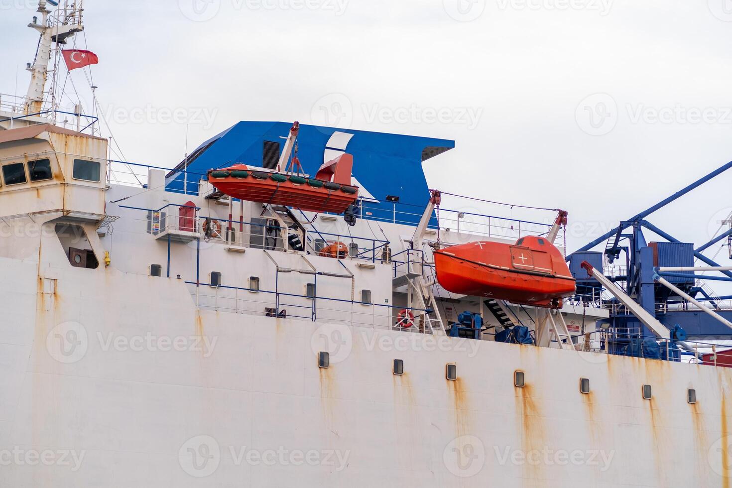 View of a cargo ship at Bosphorus with lifeboats prepared for emergency situations and colorful structures against a cloudy sky photo