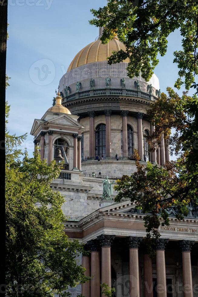 St. Isaacs Cathedral stands tall under a clear blue sky in St. Petersburg, showcasing its stunning architecture and golden dome surrounded by trees photo