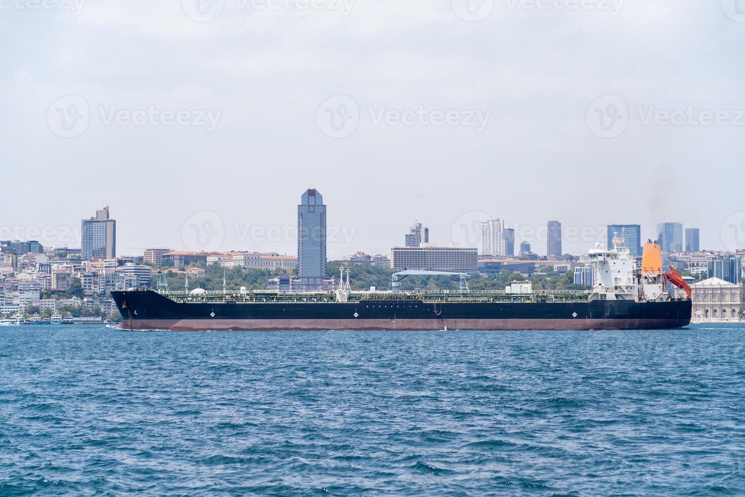 Cargo ship navigating the Bosphorus with a modern skyline in the background during a clear day photo