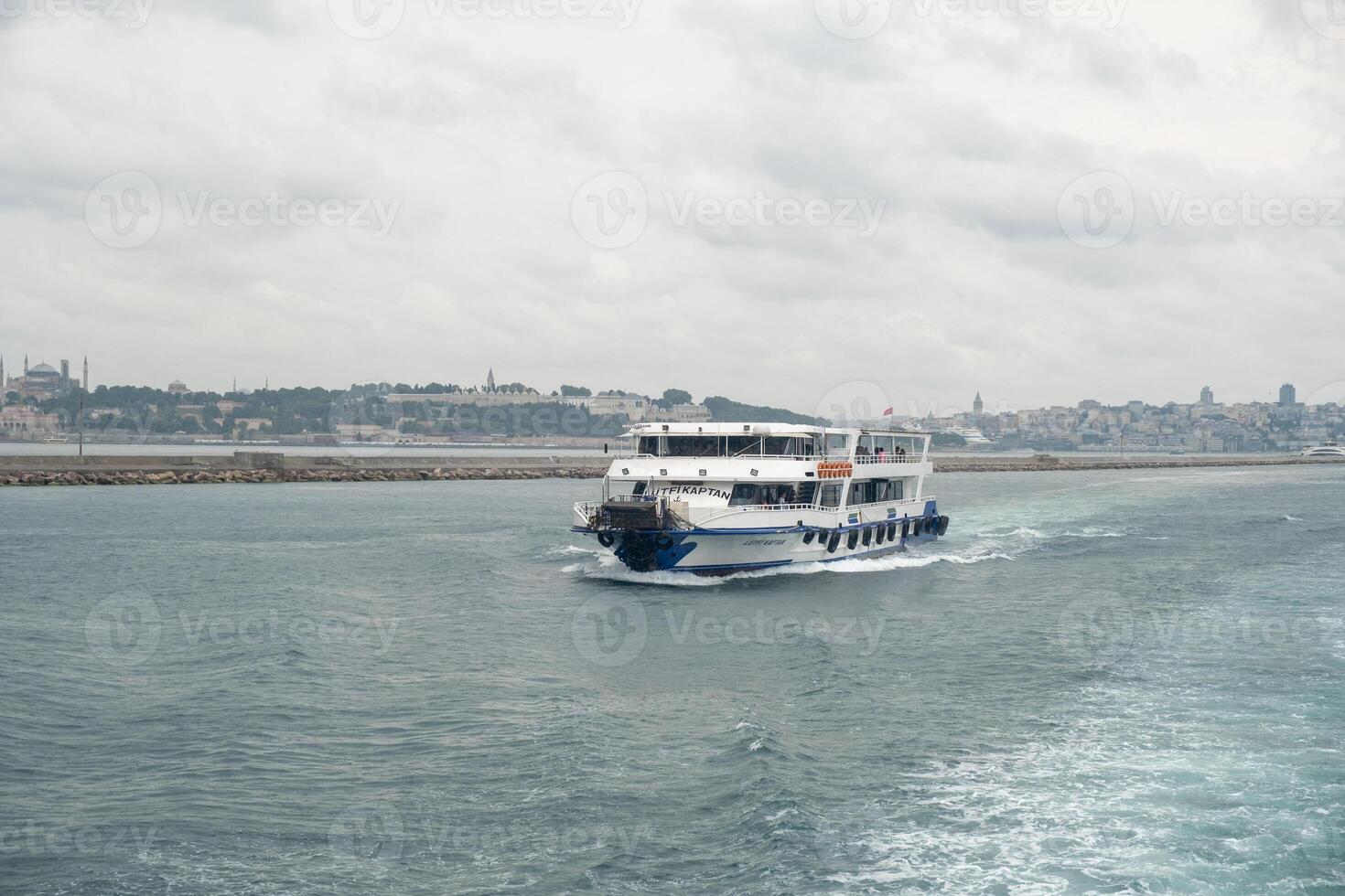 Boat navigating the Bosphorus Strait with Istanbuls skyline in the background during a cloudy afternoon photo