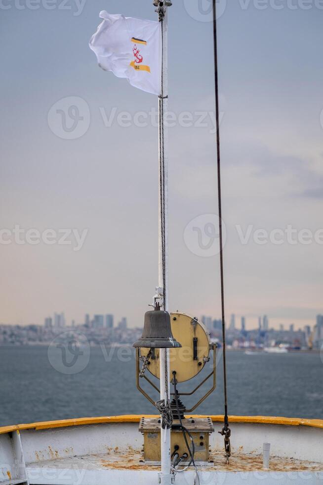 Bosphorus view from a boat with flag flying and bell in foreground on a calm and cloudy day photo