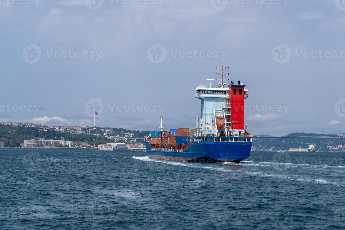 Container ship navigates Bosphorus Strait with city skyline in the background under clear skies photo