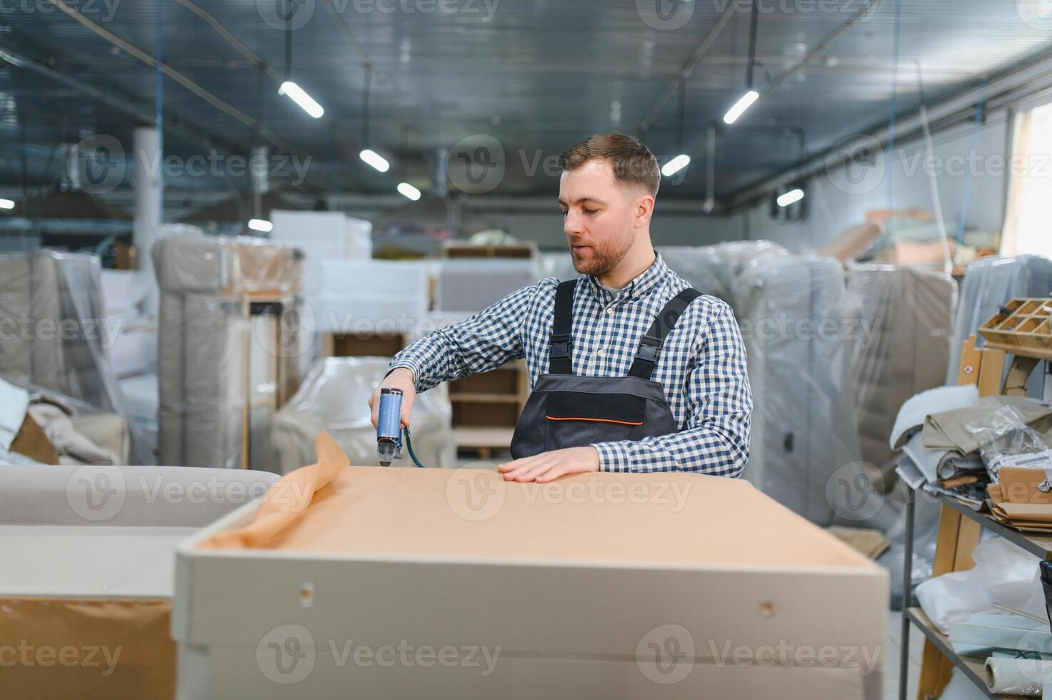 Carpenter using nail gun in furniture factory, assembling sofa frame photo
