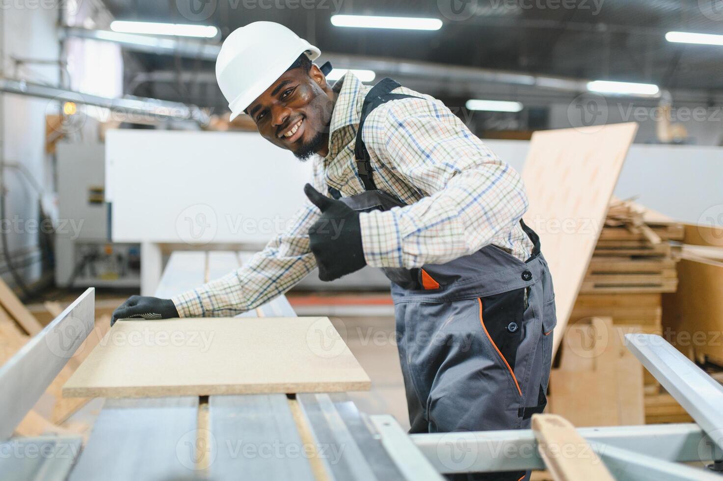 African american Carpenter gesturing thumbs up while working with wood panel in furniture factory photo