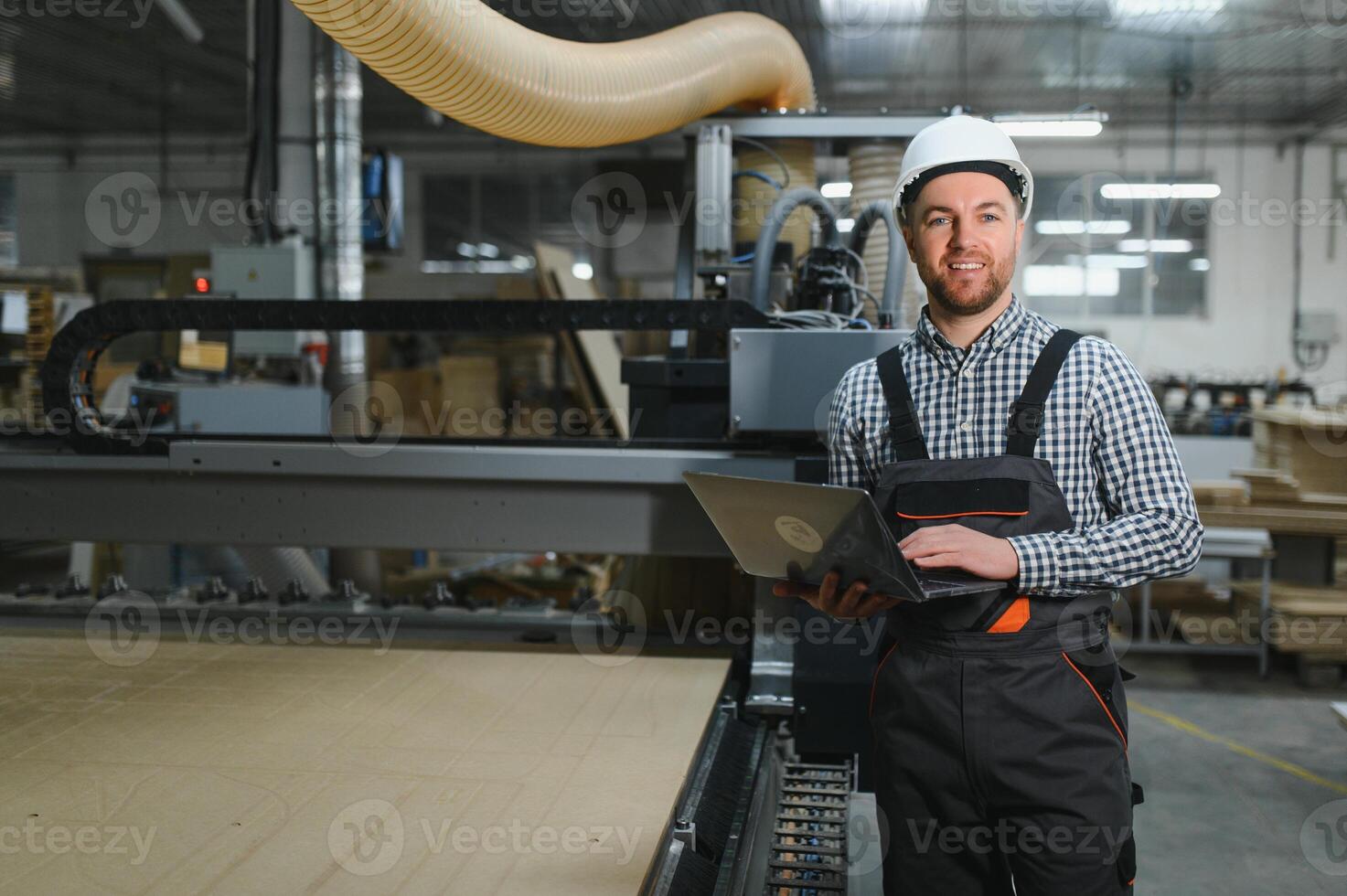 Furniture maker operating cnc wood router machine with laptop in factory photo