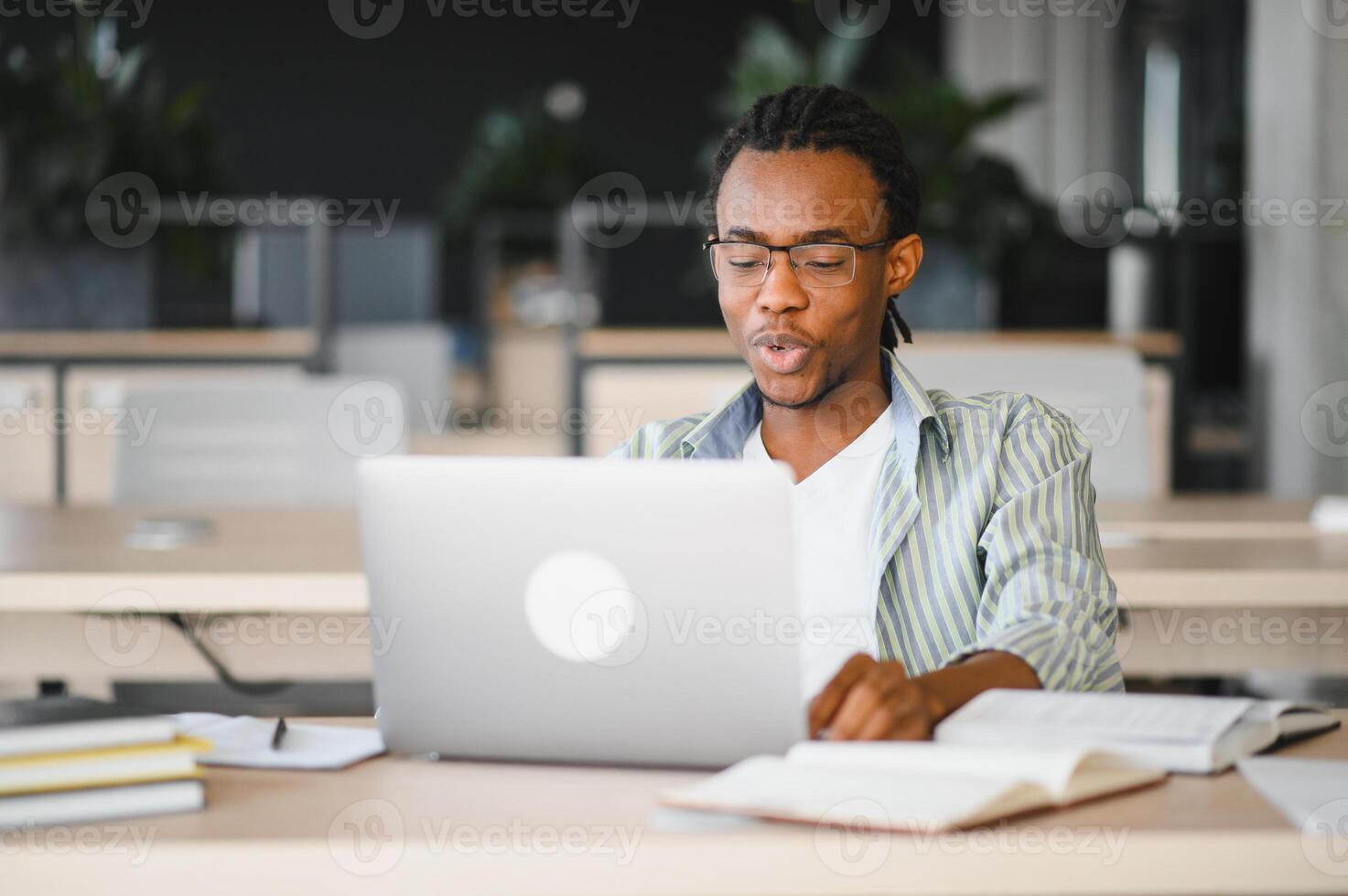 Focused university student studying with laptop and books in library photo