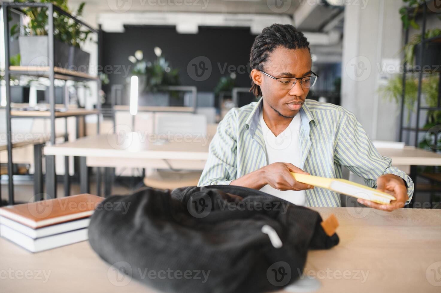 University student taking book from backpack in library study room photo