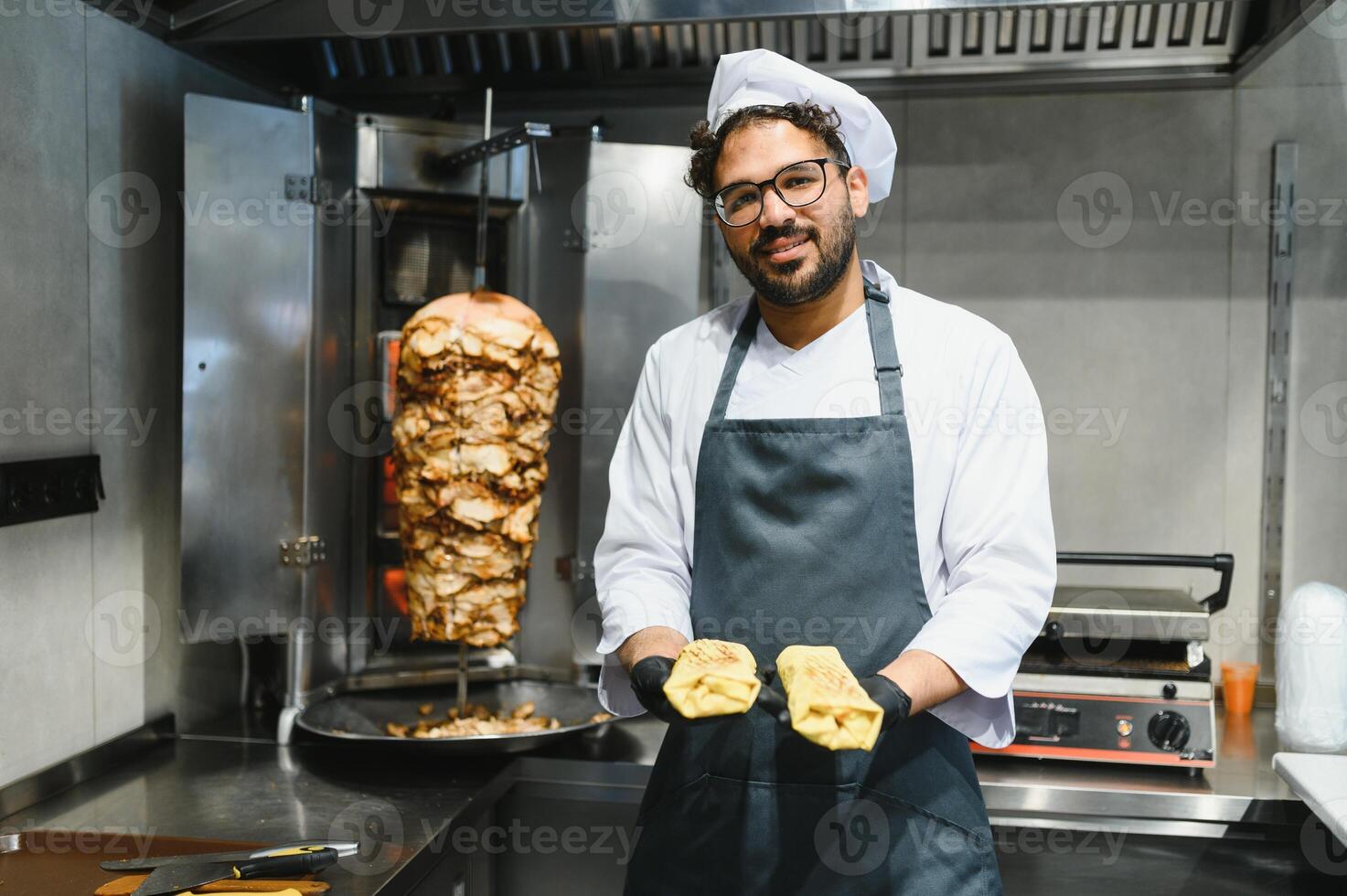 Chef holding two shawarmas next to a doner kebab machine photo