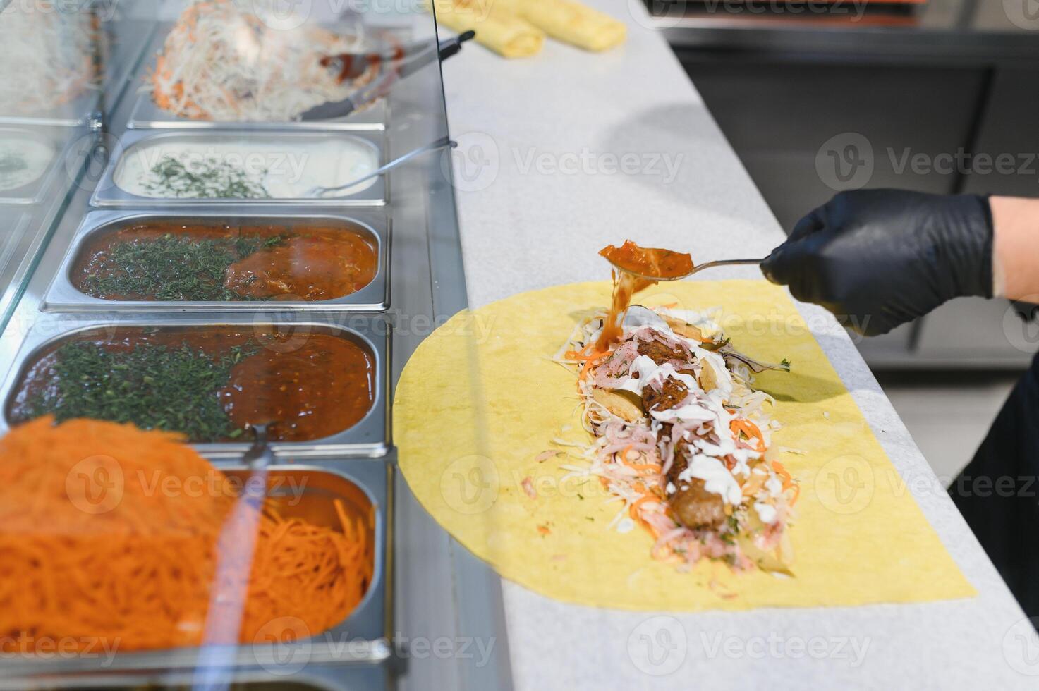 Chef adding sauce to shawarma or kebab with ingredients in food stall photo