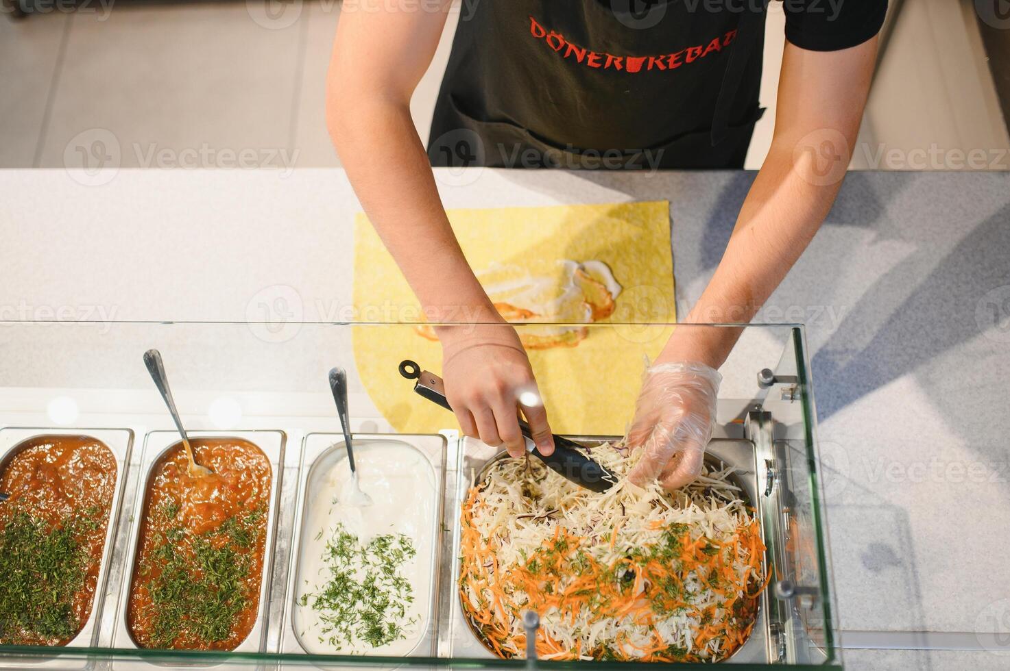 Chef adding cabbage and carrot salad to doner kebab with metal tongs photo
