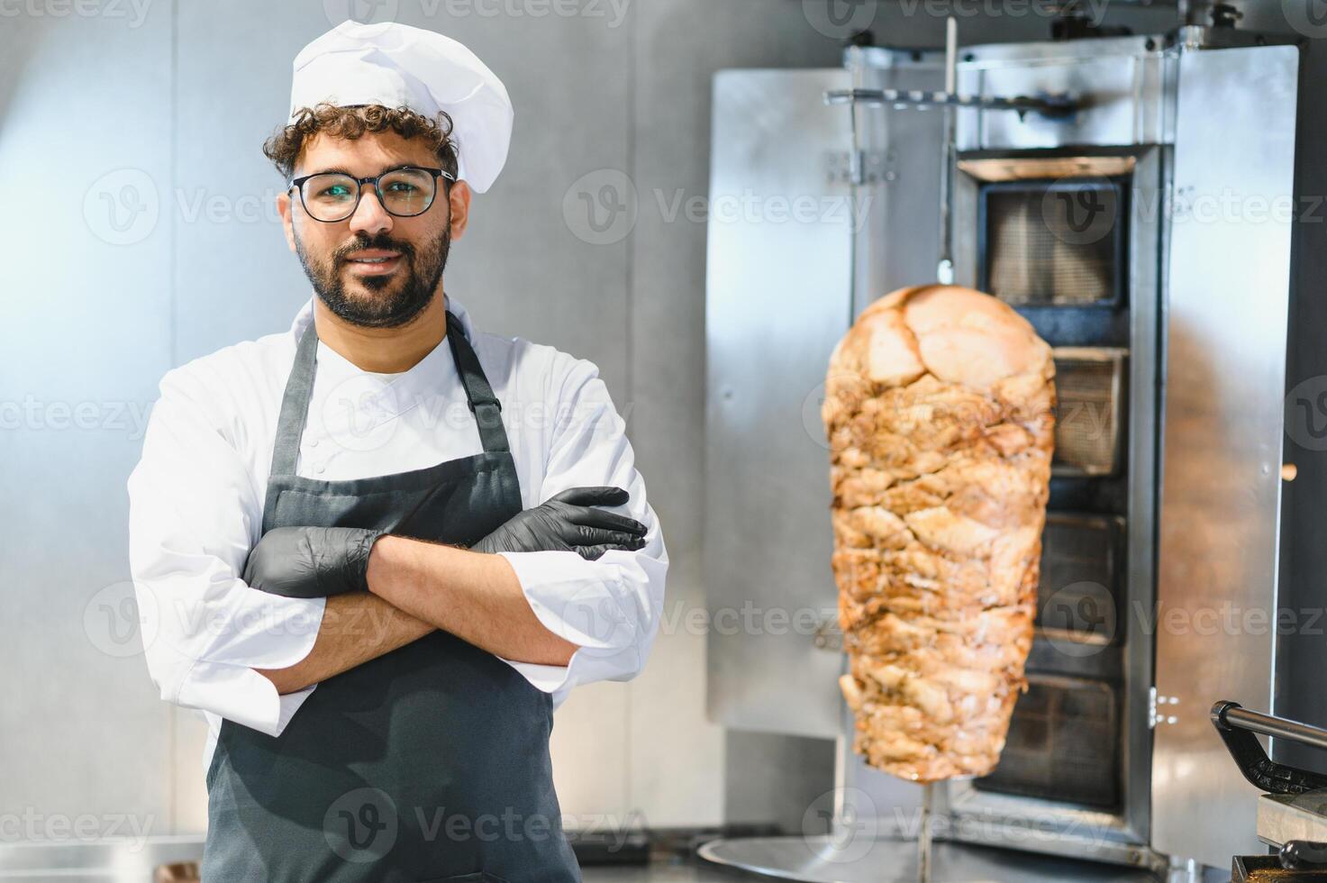 Chef smiling with crossed arms in front of shawarma machine photo