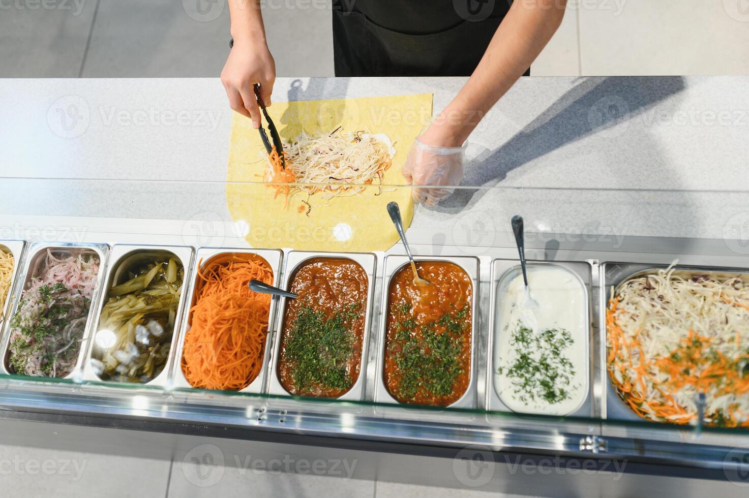 Chef adding grated carrots to shawarma with metal tongs in a street food stall photo