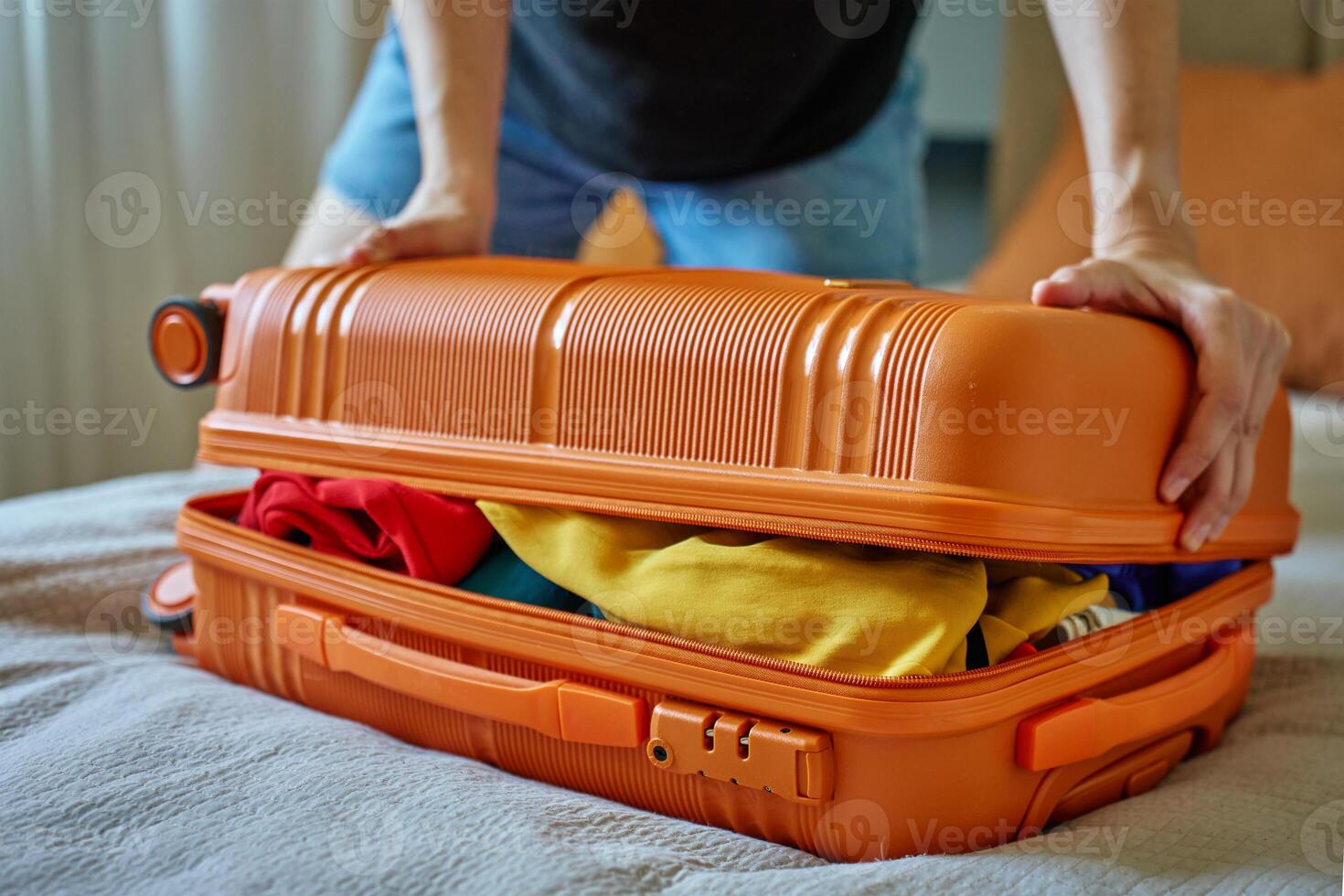 Woman trying to close suitcase. Female press down overfilled orange suitcase while packing clothes. Person preparing for departure photo