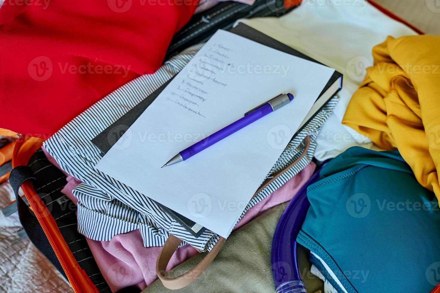 Checklist and pen on clothes packed into suitcase. Preparing for travel. Holiday and vacation planning photo
