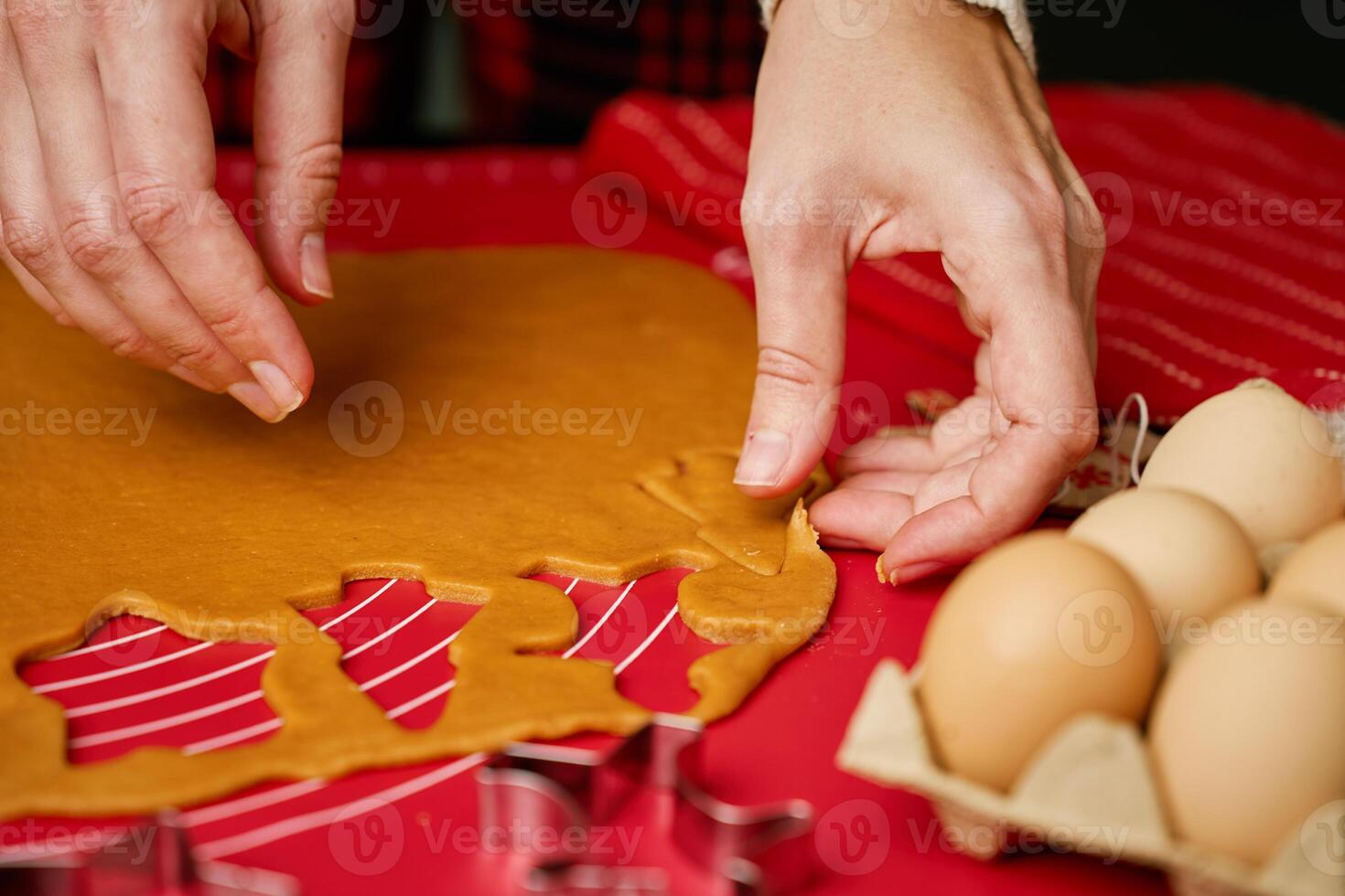 Woman using cookie cutters to shape gingerbread dough on red mat. Baking traditional Christmas cookies in home kitchen photo