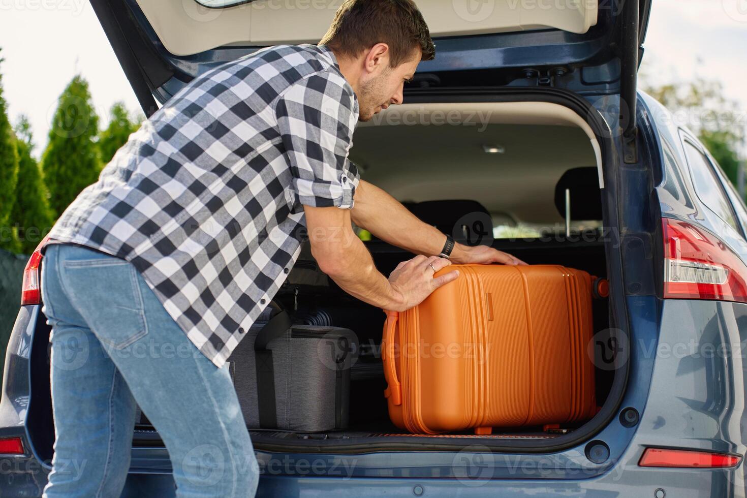 Man loading suitcase into car trunk before journey. Packing luggage for travel photo