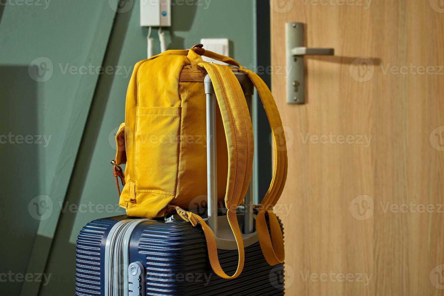 Packed dark suitcase and yellow backpack stand by door. Luggage ready for departure. Preparation for trip or travel photo