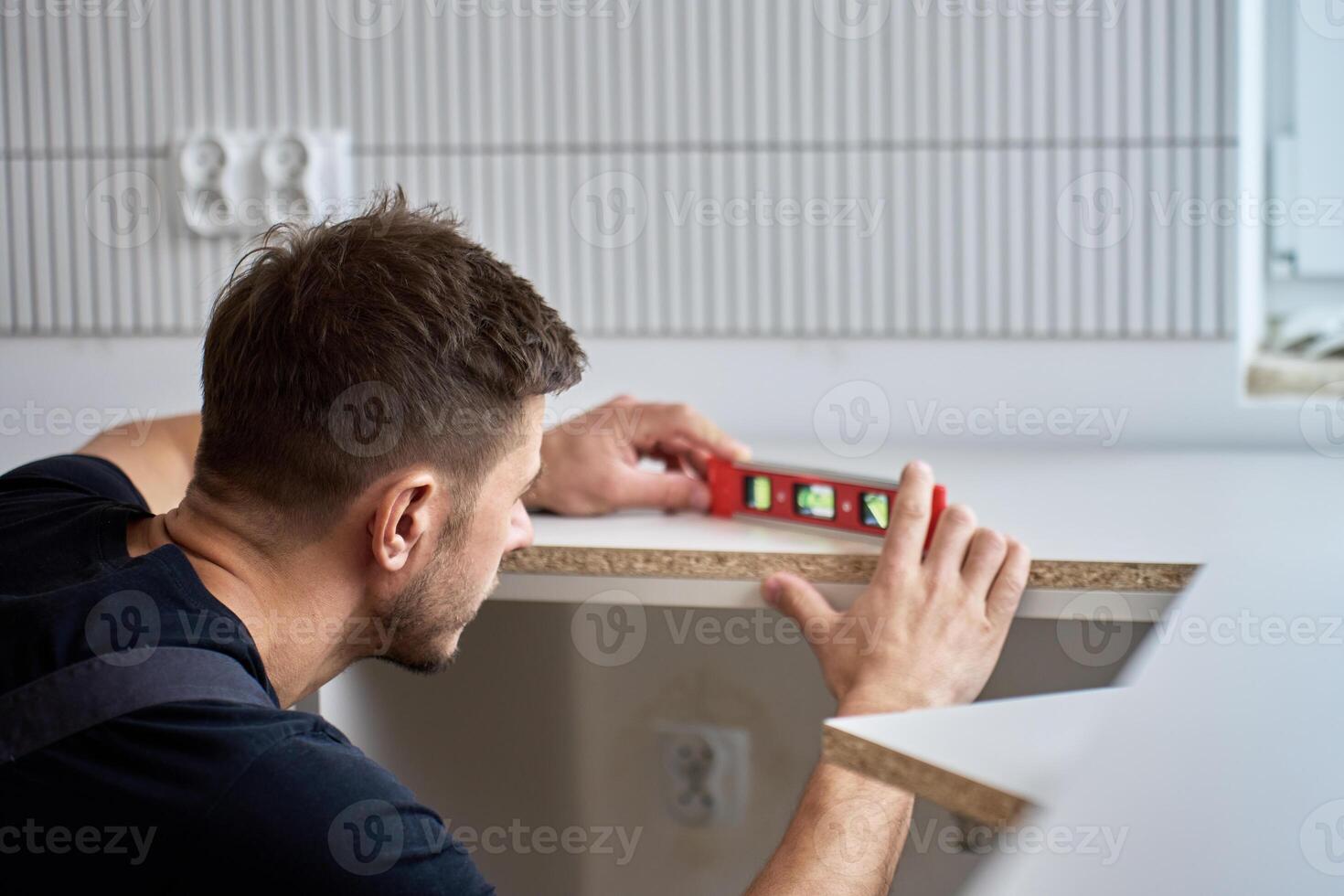 Man using spirit level to align kitchen countertop panel during installation. Professional kitchen furniture assembly during renovation in new home photo