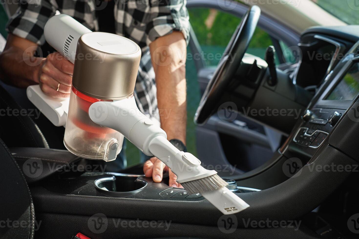 Man is vacuuming dirty car interior using handheld cordless vacuum cleaner. Car owner care about vehicle, cleaning seat upholstery and interior . Vehicle daily cleaning for comfort and hygiene photo
