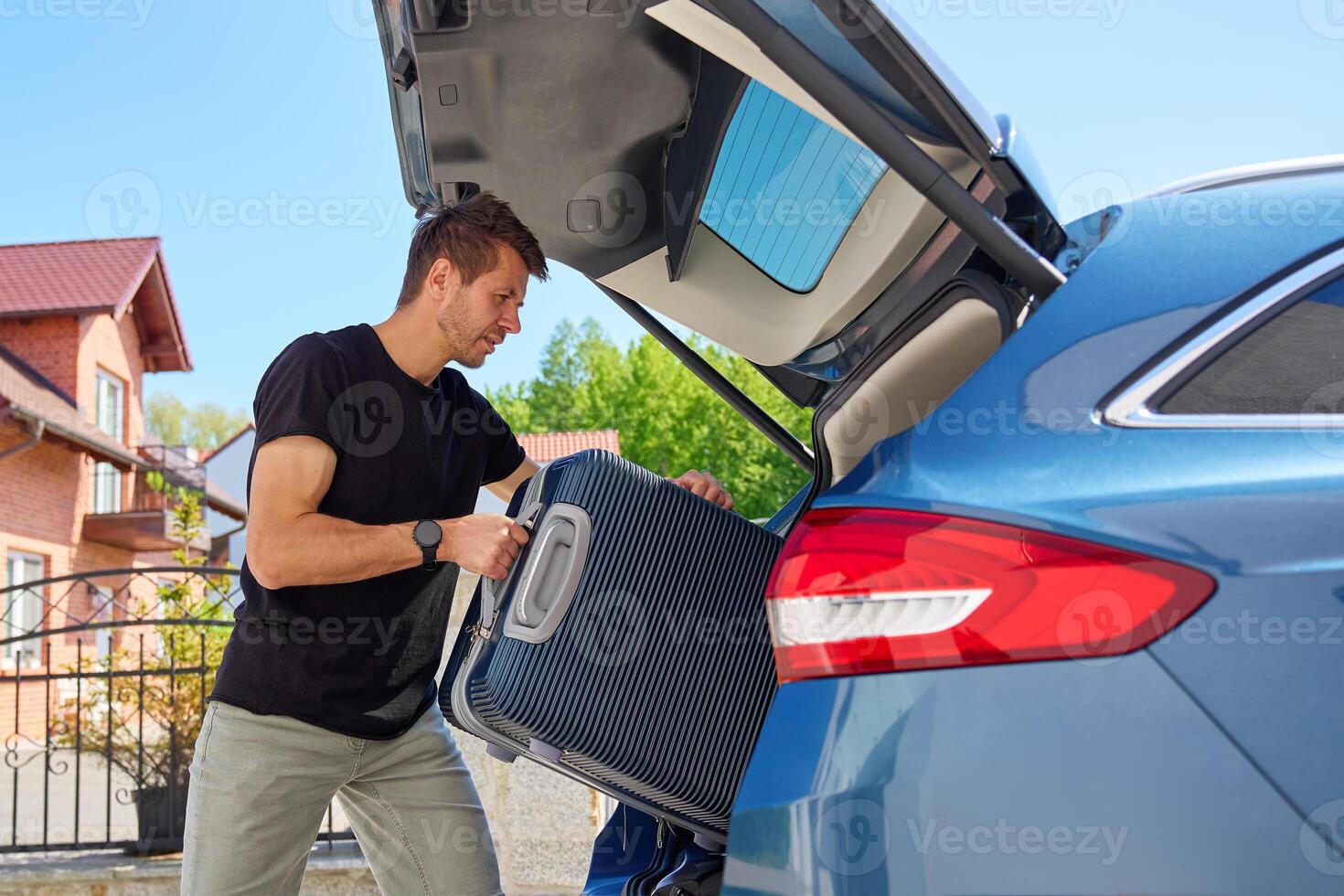 Man loading suitcase into car trunk on sunny day. Concept of preparing for summer travel, vacation or road trip with luggage photo
