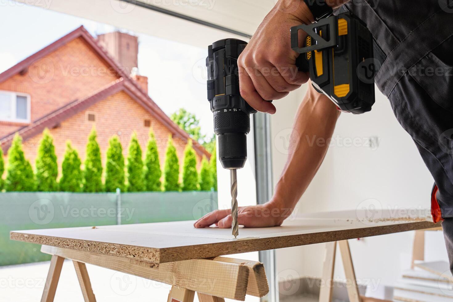 Man in using cordless power drill to make hole in laminated wood board. Male carpenter working in home workshop, drilling chipboard on workbench photo