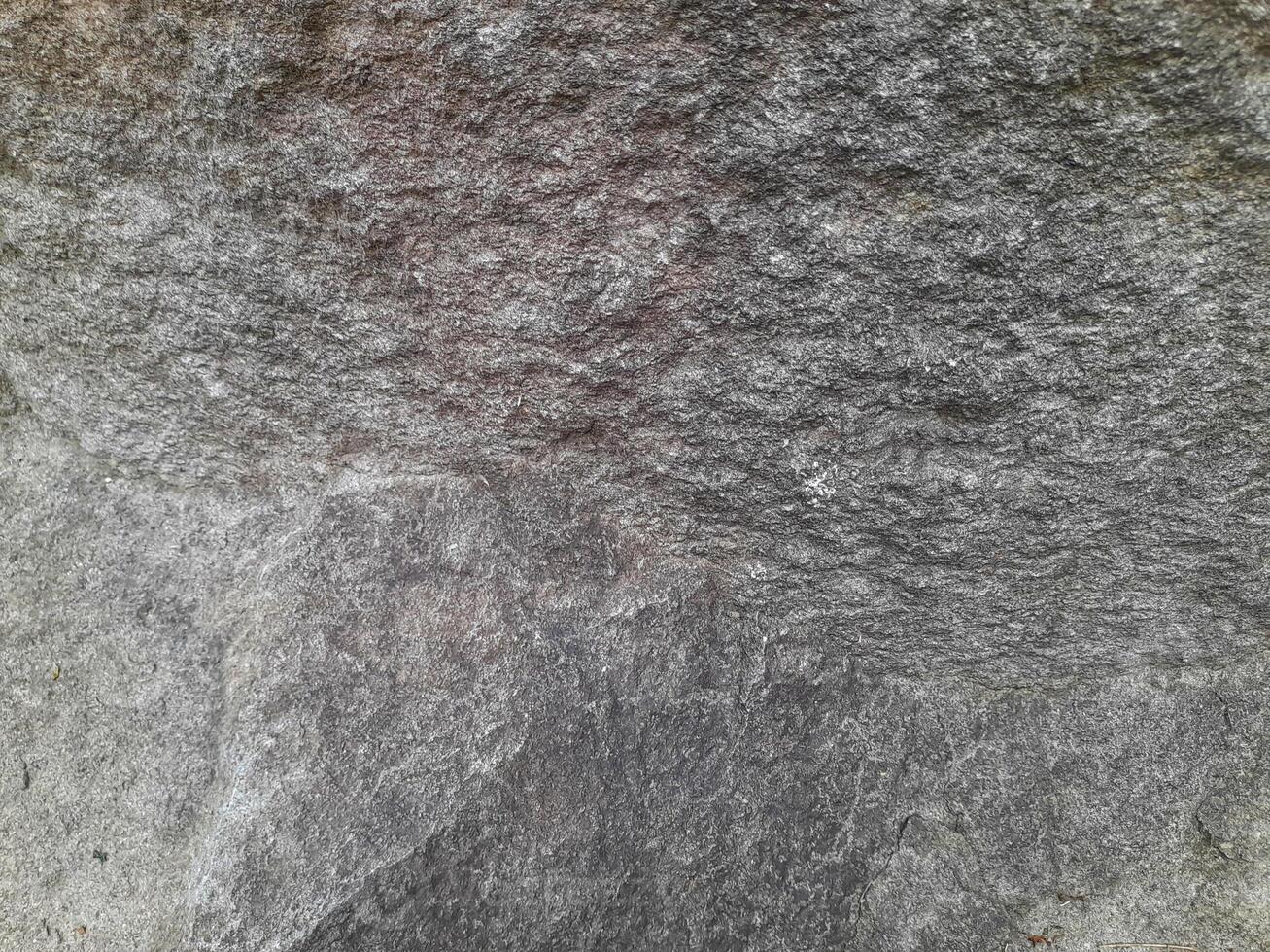 Close-up of a natural rock surface with a rough, uneven texture, visible cracks, and earthy tones, showing signs of weathering and mineral deposits photo
