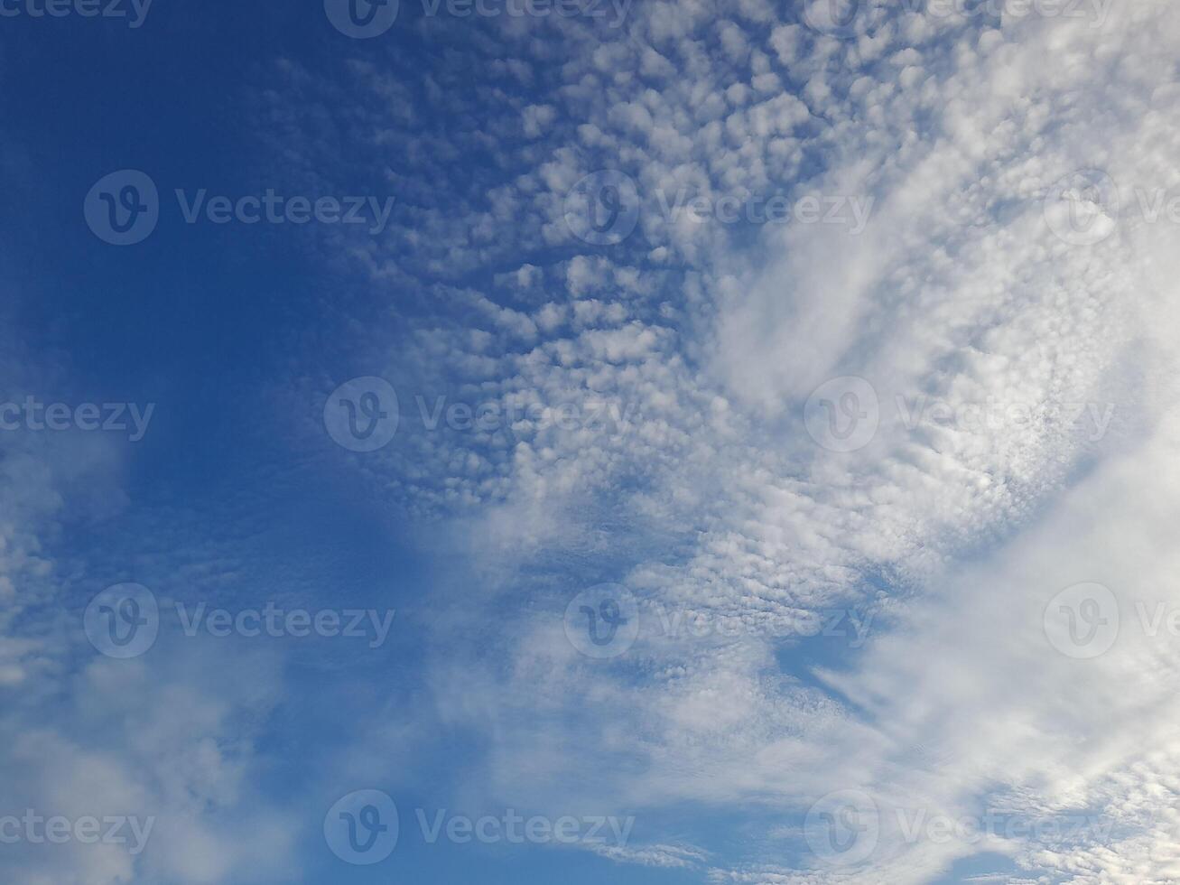 A serene sky filled with soft, scattered white clouds under a bright blue backdrop, evoking calm and peaceful vibes. photo